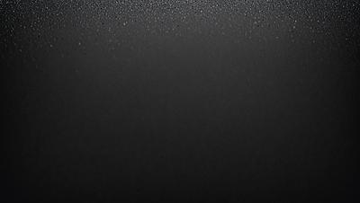 The primary subject of the image is a black background with a few specks of light, giving it a slightly textured appearance. The setting is a dark room, and the visual style is a close-up of the black background. The colors and mood of the image are predominantly dark and moody, with the black background being the main focus.