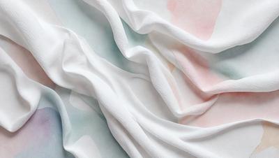The primary subject of the image is a white sheet of fabric, which is the main object in the scene. The setting is a white background, and the visual style is a close-up of the fabric. The colors and mood of the image are predominantly white, giving it a clean and minimalist appearance.