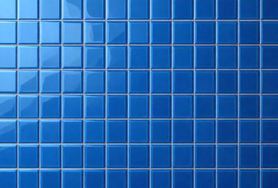 The primary subject of the image is a blue tile wall with a pattern of blue squares. The setting is a bathroom, as indicated by the blue tiles. The visual style is a close-up of the tiles, showcasing the intricate pattern and design. The dominant colors are blue, and the overall atmosphere is clean and modern.