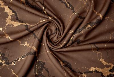 The primary subject of the image is a brown fabric with a gold pattern. The setting is a marbled surface, which adds to the visual style of the image. The colors and mood of the image are warm and earthy, with the gold pattern creating a sense of luxury and sophistication.