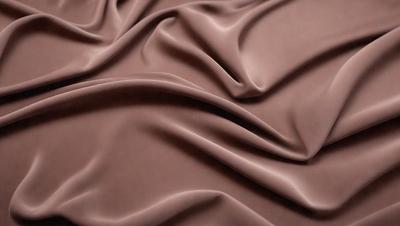 The primary subject of the image is a close-up of a brown fabric, possibly a piece of velvet or a similar material. The setting is a surface, possibly a table or a piece of furniture, where the fabric is placed. The visual style of the image is a close-up, focusing on the details of the fabric. The colors and mood of the image are predominantly brown, giving it a warm and cozy atmosphere.