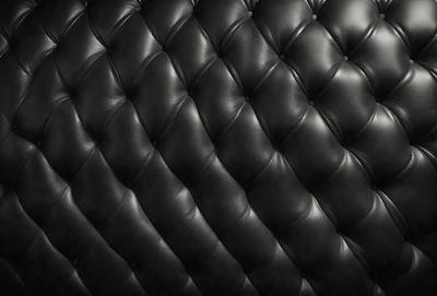 The primary subject of the image is a black leather couch. The setting is a room with a black background, which creates a striking contrast with the couch. The visual style is a close-up of the couch, showcasing its texture and details. The colors and mood of the image are predominantly black, giving it a sleek and modern appearance.