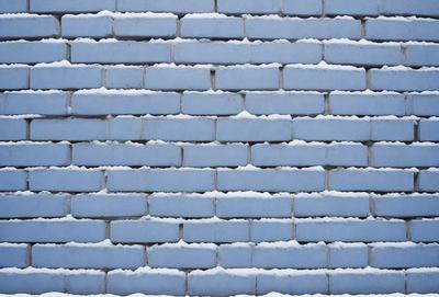 The primary subject of the image is a blue brick wall. The setting is a brick wall with snow on it, creating a wintery atmosphere. The visual style is a photo, capturing the brick wall and the snowy surface. The dominant colors are blue and white, with the blue brick wall and the white snow creating a striking contrast.