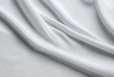 The primary subject of the image is a white sheet of fabric. The setting is a white background, which creates a clean and minimalist appearance. The visual style is a close-up of the fabric, showcasing its texture and details. The colors and mood of the image are predominantly white, giving it a calm and serene atmosphere.