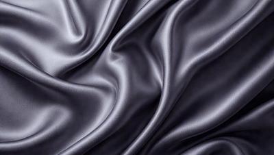 The primary subject of the image is a close-up of a piece of fabric, which appears to be a black silk material. The setting is a dark background, which emphasizes the fabric's texture and color. The visual style is a close-up, focusing on the details of the fabric. The colors and mood of the image are dark and moody, with the black silk material creating a dramatic and sophisticated atmosphere.