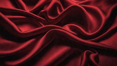 The primary subject of the image is a red fabric, possibly a piece of silk, with a flowing and ruffled texture. The setting is a dark background, which contrasts with the vibrant red color of the fabric. The visual style appears to be a close-up of the fabric, showcasing its intricate texture and details. The colors and mood of the image are predominantly red, creating a bold and striking appearance.
