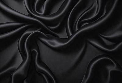 The primary subject of the image is a close-up of a black fabric, possibly a piece of clothing or a curtain. The setting is a dark background, which emphasizes the fabric's texture and color. The visual style appears to be a photo, as it captures the details of the fabric. The colors and mood of the image are predominantly dark, with the black fabric being the main focus.