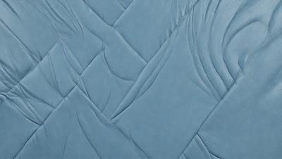 The primary subject of the image is a blue quilted fabric. The setting is a close-up view of the fabric, showcasing its texture and design. The visual style is a detailed, up-close representation of the fabric. The colors and mood of the image are predominantly blue, creating a calm and soothing atmosphere.
