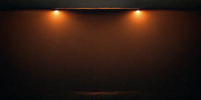 The primary subject of the image is a light source, which appears to be a light bulb or a light fixture. The light source is located in the upper left corner of the image. The setting is a dark room, with a foggy or hazy atmosphere. The visual style of the image is a black and white photo, which adds to the dramatic and moody ambiance. The colors and mood of the image are predominantly dark and mysterious, with the light source serving as a focal point amidst the