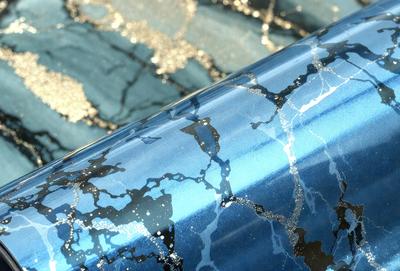 The primary subject of the image is a blue and black patterned material, possibly a piece of fabric or a wallpaper. The setting is a room with a blue background, which complements the blue and black pattern. The visual style appears to be a combination of a photo and digital art, as the pattern is intricate and detailed. The colors and mood of the image are predominantly blue and black, creating a modern and sophisticated atmosphere.