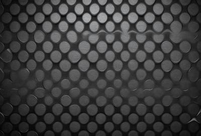The primary subject of the image is a pattern of circles, which are arranged in a grid-like formation. The setting is a black background, which contrasts with the circles, making them stand out. The visual style is a close-up of the circles, showcasing their intricate arrangement. The colors and mood of the image are predominantly black and white, giving it a clean and minimalist appearance.