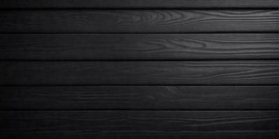 The primary subject of the image is a wooden wall. The setting is a black background, which creates a striking contrast with the wooden surface. The visual style is a close-up of the wooden wall, showcasing its texture and details. The colors and mood of the image are predominantly black, giving it a dramatic and moody atmosphere.