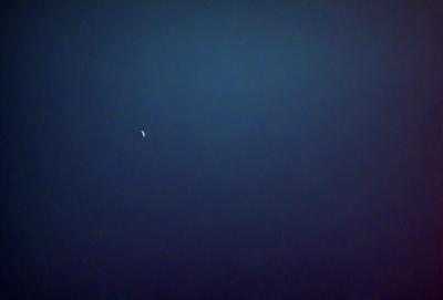 The primary subject of the image is a crescent moon, which is visible in the sky. The setting is a dark, starry night with a few stars scattered throughout the sky. The visual style is a photo, capturing the beauty of the moon and the night sky. The colors and mood of the image are predominantly dark, with the moon and stars being the main sources of light and interest.
