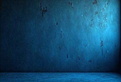 The primary subject of the image is a blue wall with a peeling paint texture. The setting is a room with a blue background. The visual style is a photo of a wall with a peeling paint texture. The dominant colors are blue and the overall atmosphere is moody and somewhat distressed.