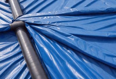The primary subject of the image is a blue tarp, which is the main object, scene, or focus of the image. The setting is an outdoor environment, with the tarp covering a surface. The visual style is a photo, capturing the tarp's texture and colors. The dominant colors are blue, and the overall atmosphere is calm and serene.