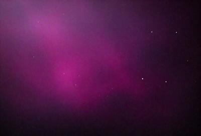 The primary subject of the image is a purple sky with a few stars visible. The setting is a dark, cloudy night with a pinkish hue. The visual style appears to be a photo, capturing the night sky with a sense of depth and atmosphere. The colors and mood of the image are predominantly purple and dark, creating a serene and mysterious ambiance.