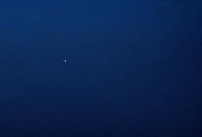 The primary subject of the image is the moon, which is visible in the sky. The setting is a dark blue sky, and the visual style appears to be a photo. The colors and mood of the image are predominantly dark and moody, with the moon being the main focal point.