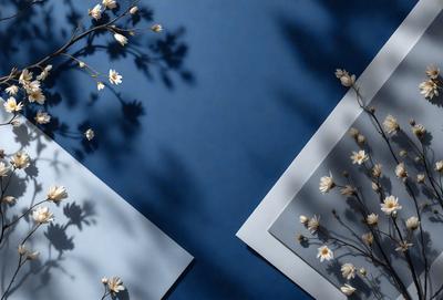 The primary subject of the image is a branch with white flowers, which is placed on a blue wall. The setting is a room with a blue background, and the visual style appears to be a photo. The colors in the image are predominantly blue and white, creating a calm and serene atmosphere.