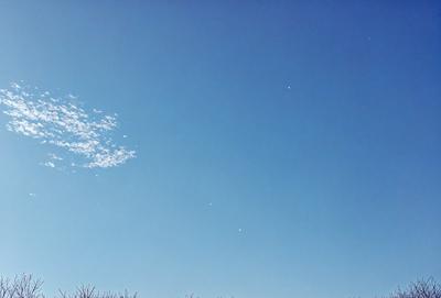 The primary subject of the image is the clear blue sky with a few white clouds scattered throughout. The setting is a vast, open space with no visible landmarks or objects. The visual style is a natural, outdoor scene with a focus on the sky and clouds. The colors and mood are predominantly blue and serene, creating a peaceful and tranquil atmosphere.