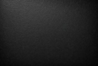 The primary subject of the image is a black leather surface. The setting is a black background, which creates a striking contrast with the leather. The visual style is a close-up of the leather, emphasizing its texture and details. The colors and mood of the image are predominantly dark, with the black leather and background creating a moody and dramatic atmosphere.
