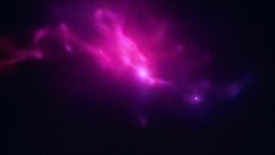 The primary subject of the image is a purple nebula, which is a cloud of gas and dust in space. The setting is a dark, starry sky, and the visual style is a combination of a photo and digital art. The dominant colors are purple and pink, creating a serene and celestial atmosphere.