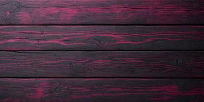 The primary subject of the image is a wooden surface with a purple tint. The setting is a wooden wall, and the visual style is a close-up of the wooden surface. The colors and mood of the image are predominantly purple, creating a unique and striking appearance.