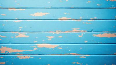 The primary subject of the image is a blue wall with peeling paint. The setting is a room with a blue wall, and the visual style is a close-up of the wall. The dominant colors are blue and white, and the overall atmosphere is somewhat aged and worn.