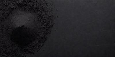 The primary subject of the image is a black substance, possibly a powder or a liquid, with a few blue specks in it. The setting is a black background, which creates a contrast with the black substance. The visual style appears to be a close-up of the black substance, possibly a photo or a digital artwork. The colors and mood of the image are predominantly dark, with the black substance and the black background creating a moody atmosphere.