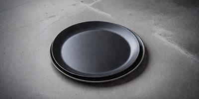 The primary subject of the image is a black plate. The plate is placed on a grey surface, which could be a table or a floor. The visual style of the image is a photo, and the colors and mood are predominantly dark and neutral.