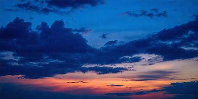 The primary subject of the image is a beautiful sunset with a cloudy sky. The setting is a picturesque landscape with a mix of clouds and a blue sky. The visual style of the image is a photo, capturing the vibrant colors and the serene atmosphere of the sunset. The dominant colors in the scene are orange, blue, and white, creating a warm and calming mood.