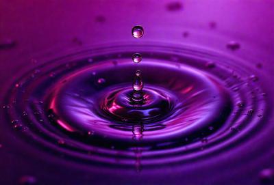The primary subject of the image is a purple water drop, which is the main focus of the scene. The setting is a purple background, which adds to the overall mood of the image. The visual style is a close-up of the water drop, showcasing its details. The colors and mood of the image are predominantly purple, creating a serene and calming atmosphere.