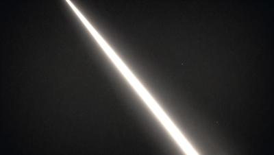 The primary subject of the image is a bright light, which appears to be a beam of light or a ray of light. The light is shining through a dark sky, creating a striking contrast between the light and the darkness. The visual style of the image is a black and white photo, which adds to the dramatic and artistic nature of the scene. The colors and mood of the image are predominantly dark, with the bright light being the main focal point and source of interest.