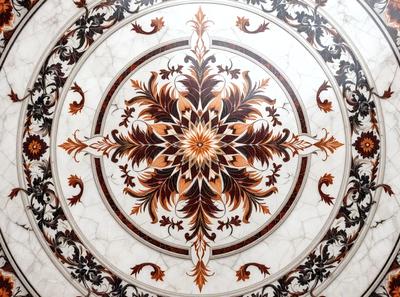 The primary subject of the image is a beautifully designed and intricately crafted marble floor. The floor features a large, ornate design with a central sun motif, surrounded by a variety of floral patterns. The setting is a room with a marble wall, which complements the floor's design. The visual style of the image is a close-up of the floor, showcasing the intricate details of the artwork. The colors and mood of the image are warm and inviting, with the mar