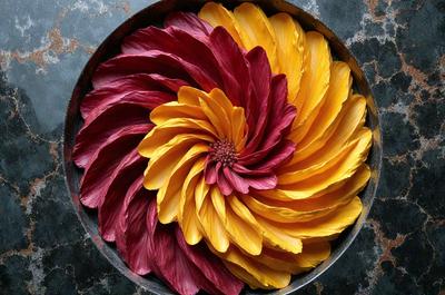 The primary subject of the image is a vibrant flower arrangement in a bowl. The flower arrangement consists of a mix of red, yellow, and orange flowers, creating a visually appealing and colorful display. The setting is a bowl placed on a table, which serves as the background for the flower arrangement. The visual style of the image is a close-up of the flower arrangement, highlighting the details and colors of the flowers. The dominant colors in the image are red, yellow, and orange, creating a warm and