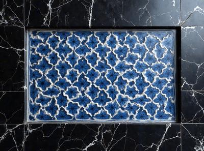 The primary subject of the image is a blue and white tile with a pattern of flowers. The setting is a black marble countertop, and the visual style is a close-up of the tile. The colors and mood of the image are predominantly blue and white, creating a clean and elegant atmosphere.