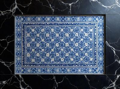 The primary subject of the image is a blue and white tiled floor. The setting is a room with a black marble countertop. The visual style is a photo of the tiled floor. The colors and mood of the image are predominantly blue and white, creating a clean and elegant atmosphere.