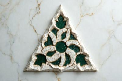 The primary subject of the image is a decorative tile with a green and white design. The tile is placed on a marble surface, which serves as the setting and background of the scene. The visual style of the image is a close-up of the tile, showcasing its intricate details. The dominant colors in the image are green and white, creating a calm and serene atmosphere.