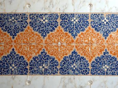 The primary subject of the image is a blue and orange tile design. The setting is a wall with a marble surface, and the visual style is a patterned tile design. The dominant colors are blue and orange, creating a vibrant and lively atmosphere.