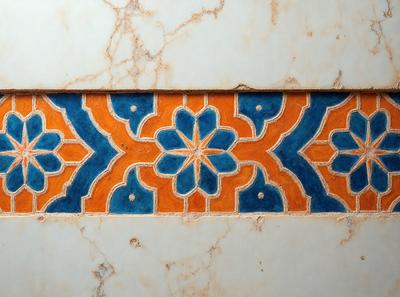 The primary subject of the image is a decorative tile with a blue and orange floral pattern. The tile is set against a white marble background, giving it a clean and elegant appearance. The visual style of the image is a close-up of the tile, showcasing its intricate design and colors. The dominant colors in the image are blue and orange, creating a vibrant and lively atmosphere.