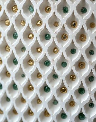 The primary subject of the image is a white and gold patterned wall. The setting is a white wall with a gold and green pattern. The visual style is a combination of photo and digital art, creating a unique and intricate design. The dominant colors are white, gold, and green, giving the wall a warm and inviting atmosphere.