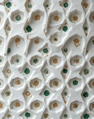 The primary subject of the image is a pattern of green and gold circles, which are arranged in a white background. The circles are of various sizes and are placed in a visually appealing manner. The setting appears to be a white wall or surface, which serves as the background for the pattern. The visual style of the image is a combination of digital art and illustration, creating a unique and eye-catching design. The colors and mood of the image are predominantly green and gold, giving it a warm and inviting atmosphere