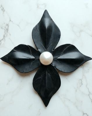 The primary subject of the image is a black flower with a pearl in the center. The flower is made of a combination of black and white materials, giving it a unique and artistic appearance. The setting is a white marble surface, which provides a clean and elegant backdrop for the flower. The visual style of the image is a blend of digital art and illustration, creating a striking and eye-catching design. The colors and mood of the image are predominantly black and white, with a touch of eleg