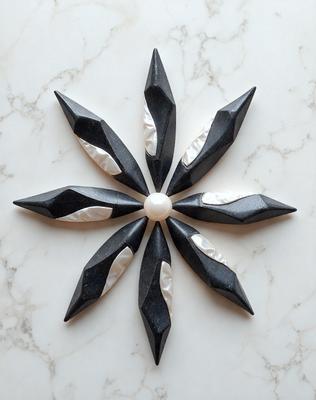 The primary subject of the image is a black and white decoration, possibly a sculpture or a piece of art, featuring a flower design. The setting is a white marble surface, which serves as the background for the decoration. The visual style of the image is a combination of photo and digital art, creating a unique and intricate design. The colors and mood of the image are predominantly black and white, giving it a classic and elegant appearance.