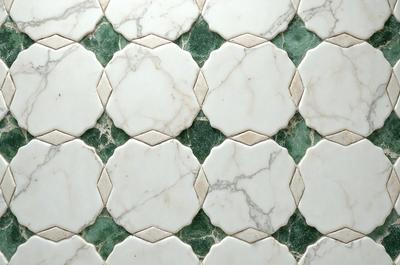 The image features a white marble tile pattern with green accents. The tiles are arranged in a diamond pattern, creating a visually appealing and unique design. The primary subject of the image is the marble tile pattern, which is the main focus of the scene. The setting is a wall or floor with the tiles covering it, and the visual style is a close-up of the tile pattern. The colors and mood of the image are predominantly white and green, giving it a clean and fresh appearance.
