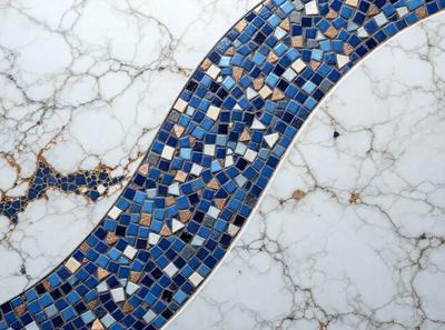 The primary subject of the image is a blue and white mosaic tile. The setting is a white marble countertop, and the visual style is a close-up of the tile. The dominant colors are blue and white, creating a clean and elegant atmosphere.