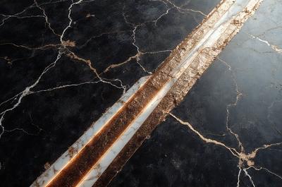 The primary subject of the image is a marble countertop with a gold stripe running through it. The setting is a kitchen or bathroom, as the countertop is a part of the room's design. The visual style is a close-up of the countertop, showcasing the gold stripe and the marble surface. The colors and mood of the image are elegant and luxurious, with the gold stripe adding a touch of sophistication to the marble countertop.