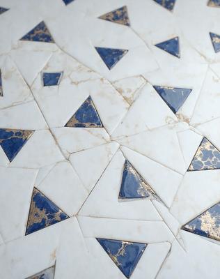 The primary subject of the image is a white and blue tile with a gold pattern. The setting is a wall, and the visual style is a patterned tile. The dominant colors are white, blue, and gold, creating a clean and elegant atmosphere.