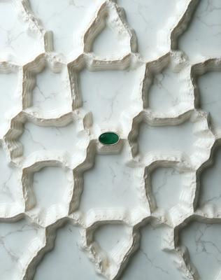 The primary subject of the image is a green gemstone, which is placed in the center of a white marble surface. The setting is a white marble tiled wall, and the visual style is a close-up of the gemstone. The colors and mood of the image are predominantly white and green, giving it a clean and fresh appearance.