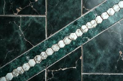 The primary subject of the image is a green and white marble tile. The setting is a bathroom, with the tile covering the floor. The visual style is a close-up of the tile, showcasing its intricate design. The colors and mood of the image are predominantly green and white, giving it a clean and elegant appearance.