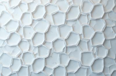 The primary subject of the image is a white wall with a pattern of white hexagons. The setting is a room with a white background, and the visual style appears to be a photo. The dominant colors are white, and the overall atmosphere is clean and minimalistic.